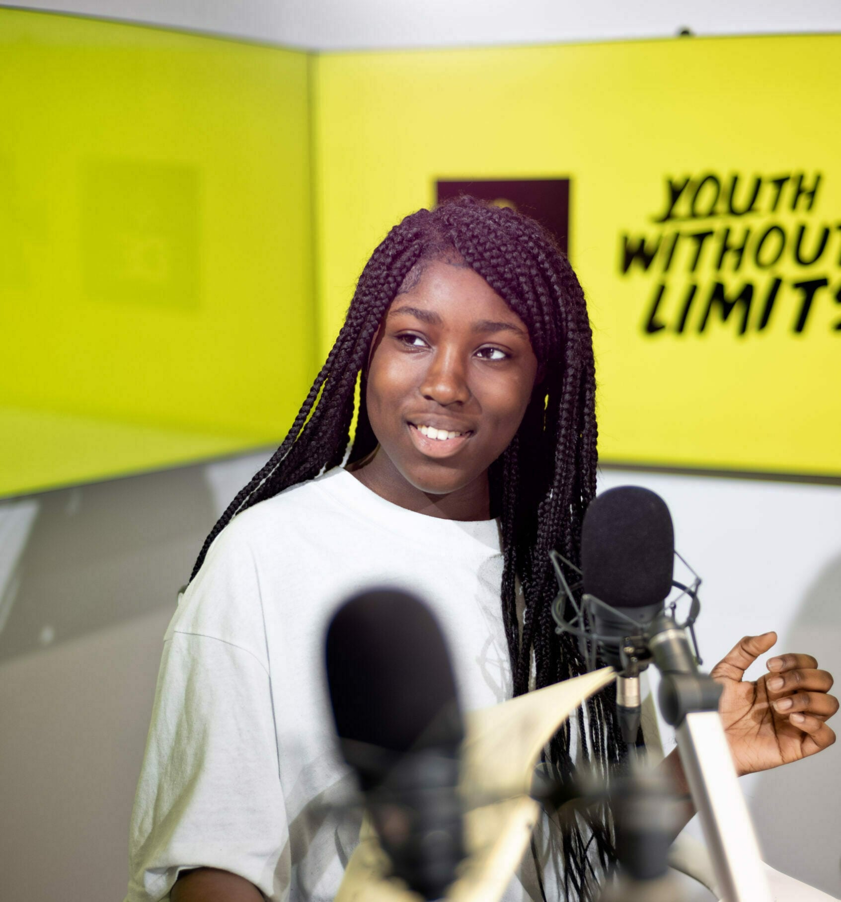 A young person standing behind two microphones with the D of E Youth without limits logo behind.