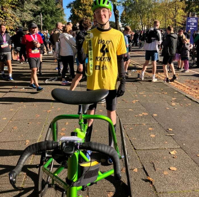 Finlay in a Do it for youth yellow t-shirt and green helmet holding a Manchester Half Marathon medal.