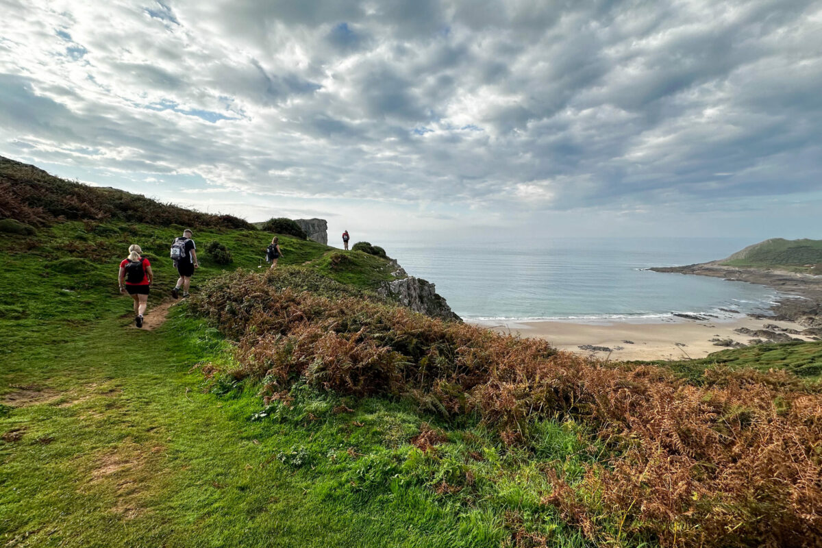 Four people walking along a path on a cliff above a beach.