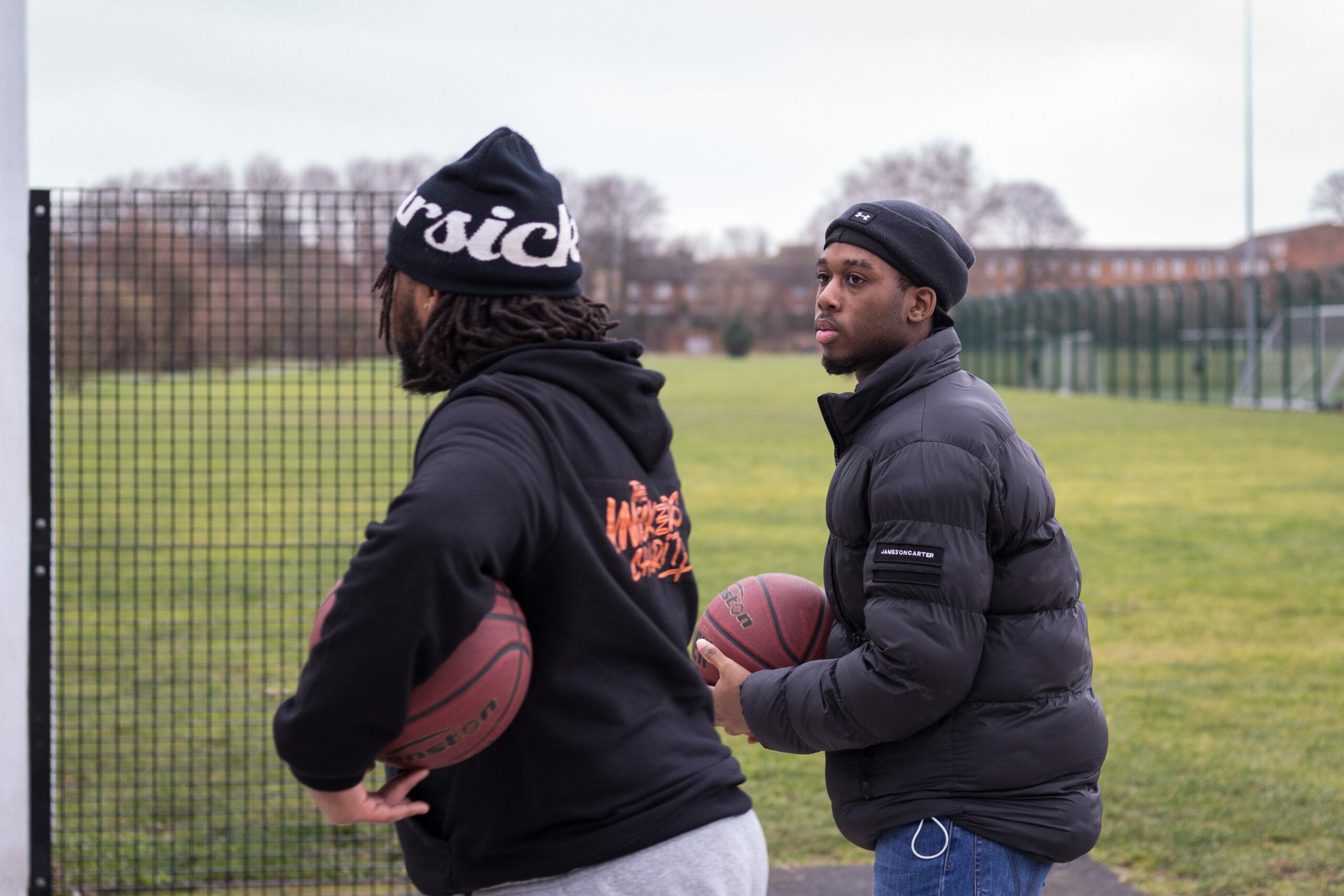 Two young people holding basketballs walking along a grassy pitch.