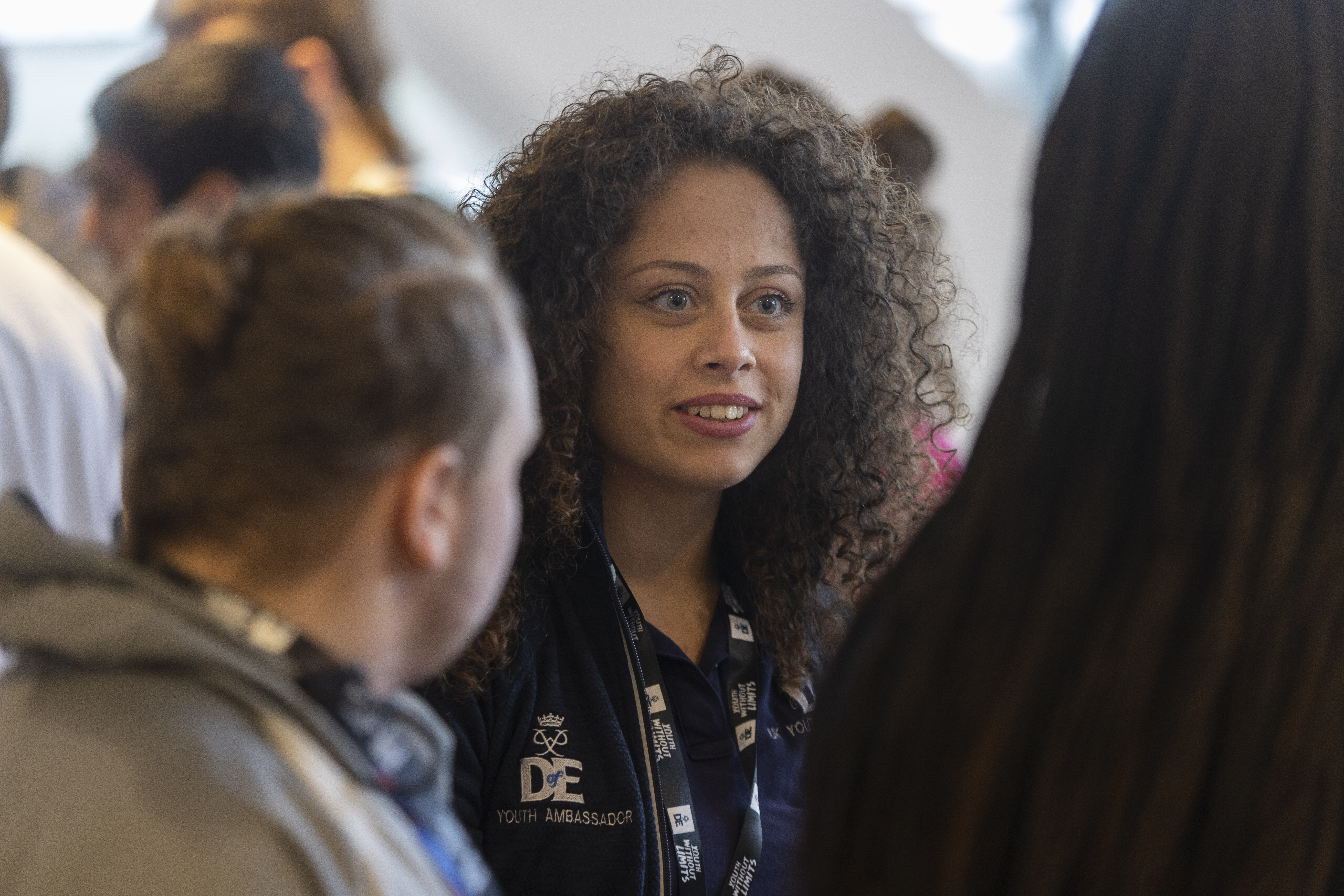 A Youth Ambassador talking to another person and looking away from the camera. She is wearing a DofE lanyard and Youth Ambassador polo shirt.