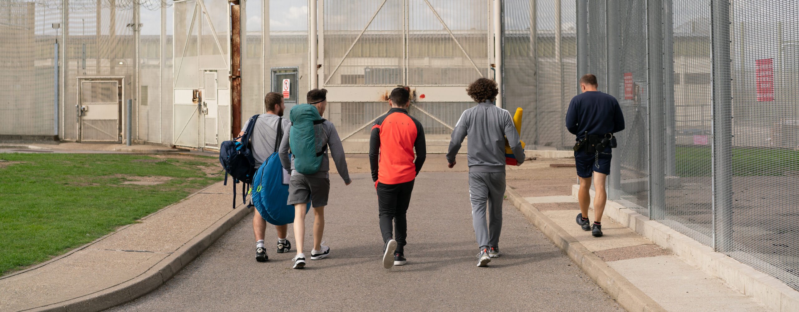 4 young offenders and a prison officer walking towards some gates.
