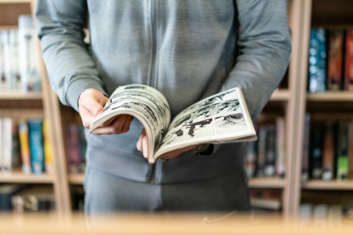 A young offender in a library holding an open book. His face is not in the frame.