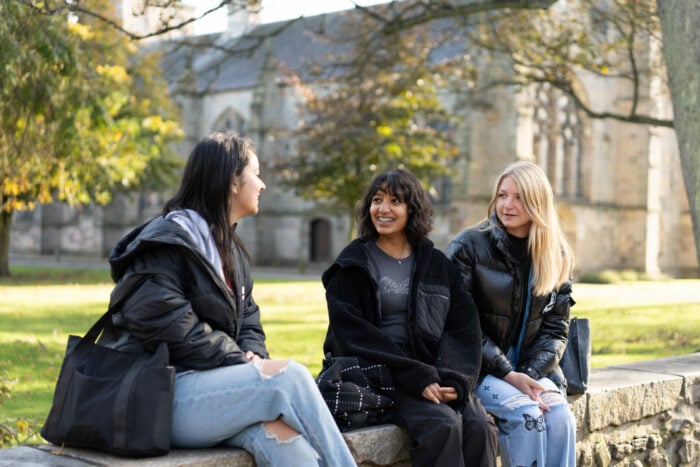Three young people sitting on a wall in front of a church. They are all laughing and making eye contact with each other.