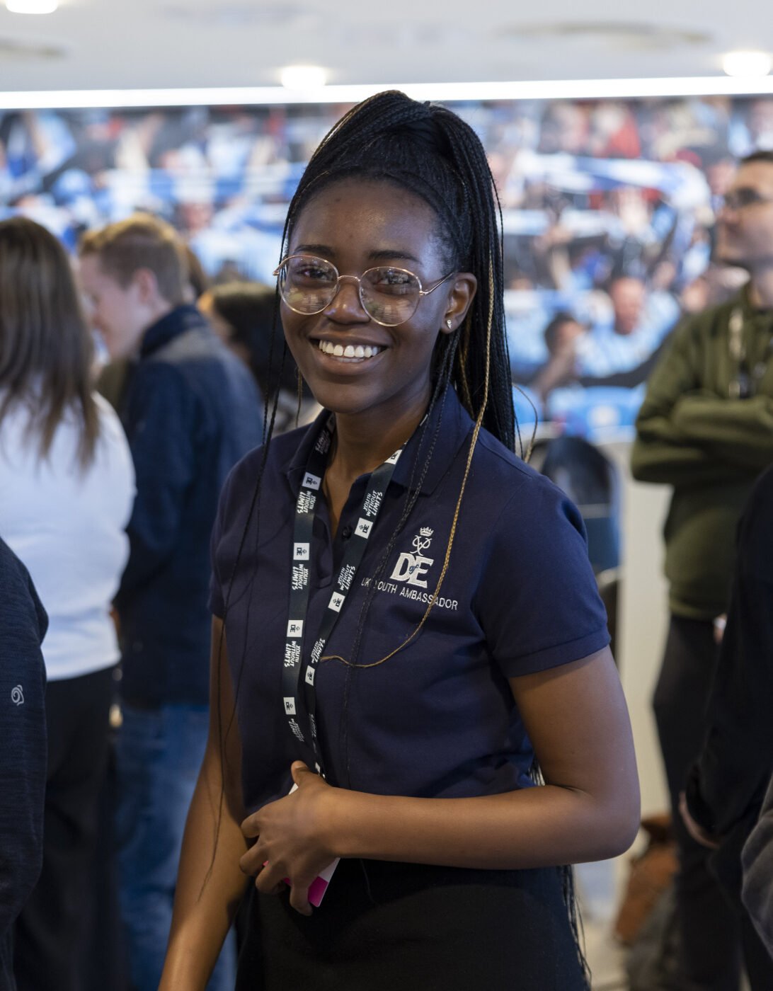 A DofE UK Youth Ambassadors smiling to camera at an event. She is wearing a DofE polo.