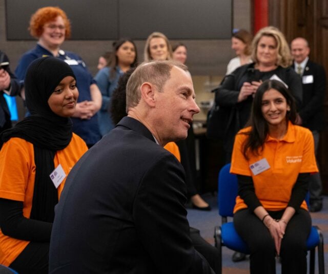 A man sits in the centre of a room surrounded by people smiling and laughing.