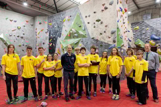 HRH The Duke of Edinburgh with a group of young people wearing yellow tops at a bouldering centre.