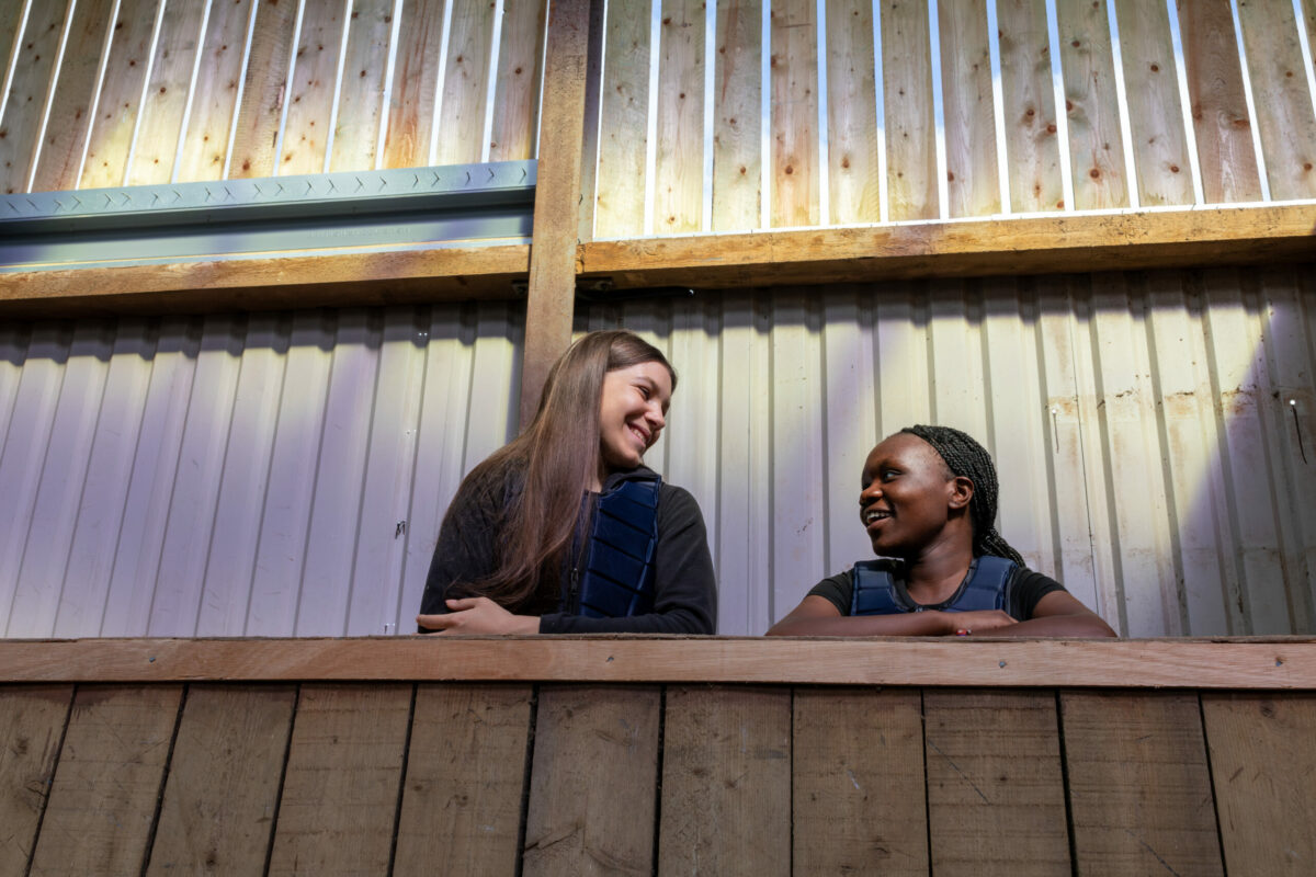Two young people leaning on a wooden ledge, smiling and chatting.