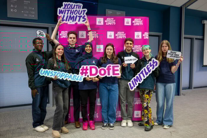 UK Youth Ambassadors stands together in a brightly lit room, smiling and holding colorful signs with motivational phrases such as 
