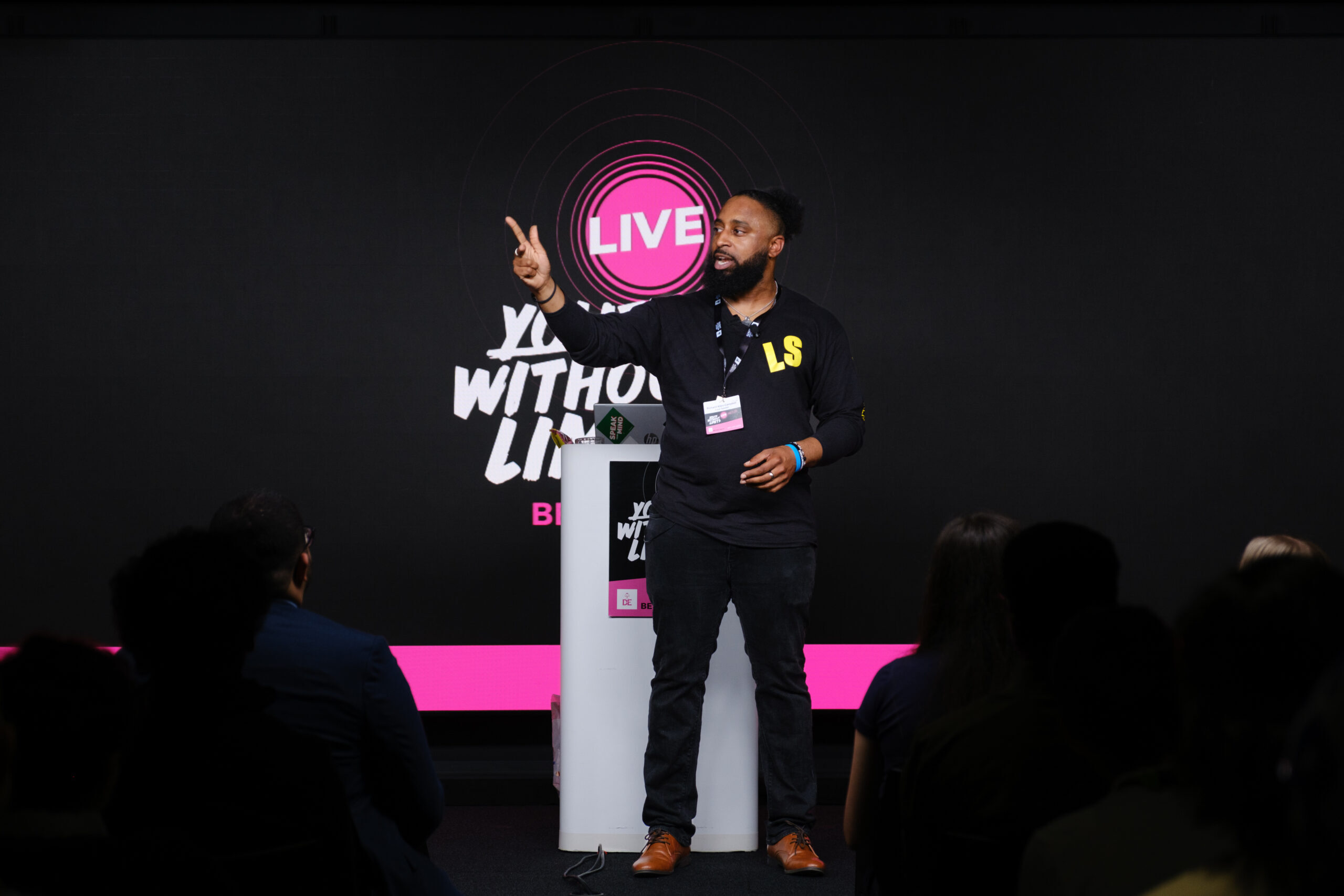 A speaker on stage at Youth Without Limits Live, his hand is in the air pointing upwards.