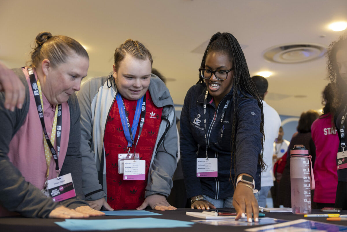 Two young people and an adult looking at pieces of paper on a table.