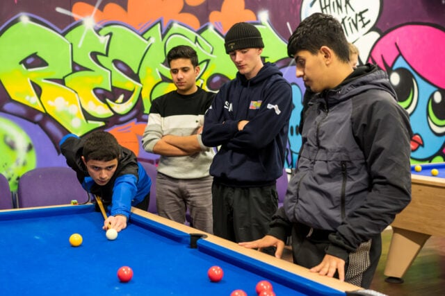 Four young people playing pool inside a room with graffiti on the walls.