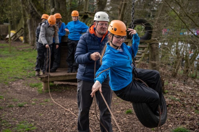 A DofE Leader helps a young person cross an outdoors assault course.