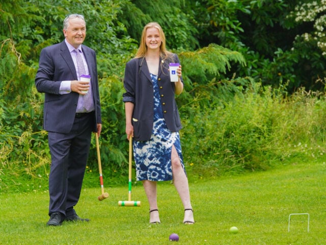 A man in a suit and a woman in a dress hold mallets and DofE cups in the Hillsborough Palace Gardens.