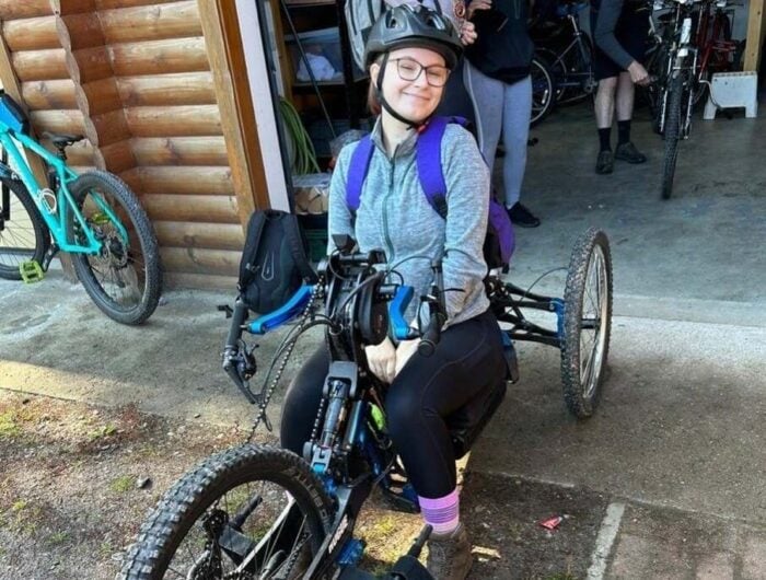 Emma sitting on a three-wheel bike wearing a helmet and smiling.