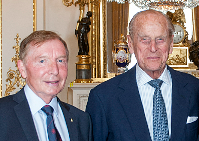HRH Prince Philip, The Duke of Edinburgh (right) stands next to Sir Tom Farmer (left) in a richly decorated room with ornate gold details, a large mirror, and antique furnishings in the background. Both men are dressed in formal suits and smiling slightly at the camera.