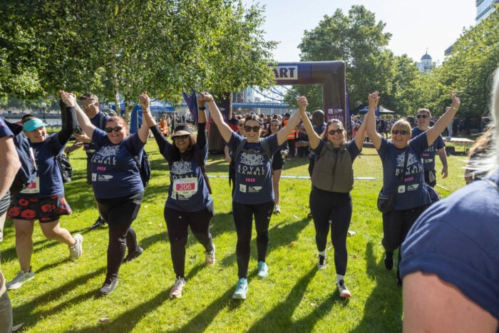 A line of people in Royal Ramble t-shirts hold hands and raise them over their heads after finishing a 20-mile walk.