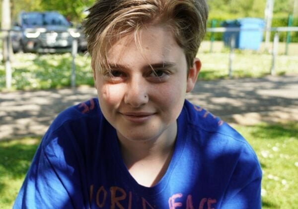 Teddy wearing a blue t-shirt looking directly at the camera. He has a lock of blonde hair over his face and a nose piercing.