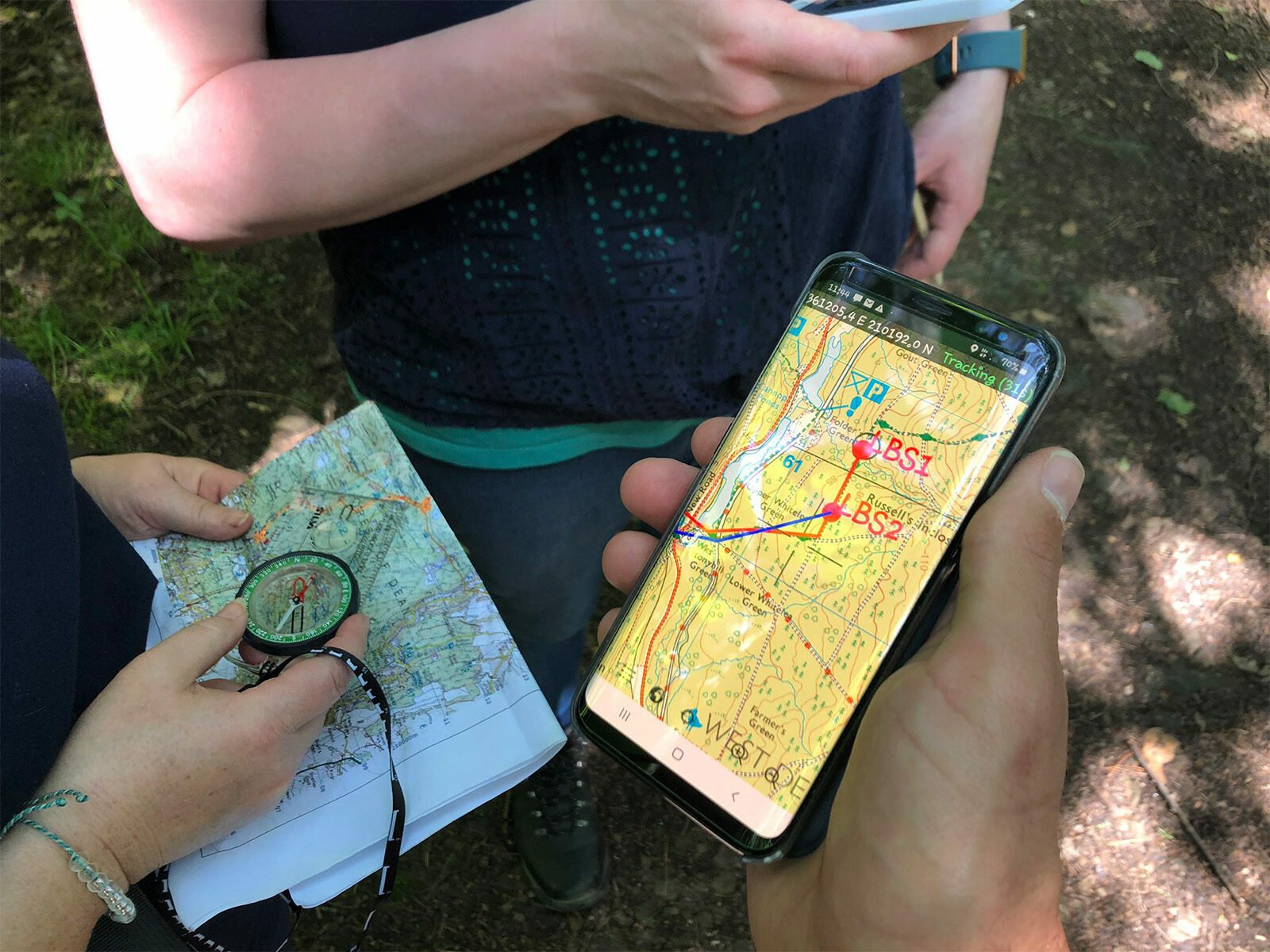 People holding a map, compass and a tracking system on their phone