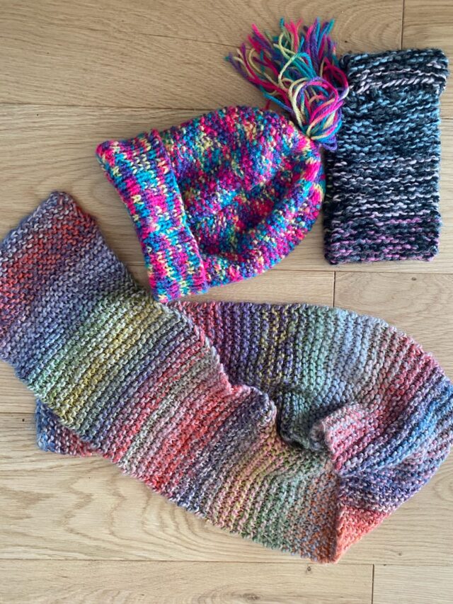 Colourful knitted scarf, hat and square lying on the ground.