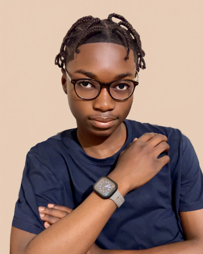 Chris wearing glasses and a dark blue shirt, posing with one arm crossed over the chest and the other hand resting on the opposite shoulder.