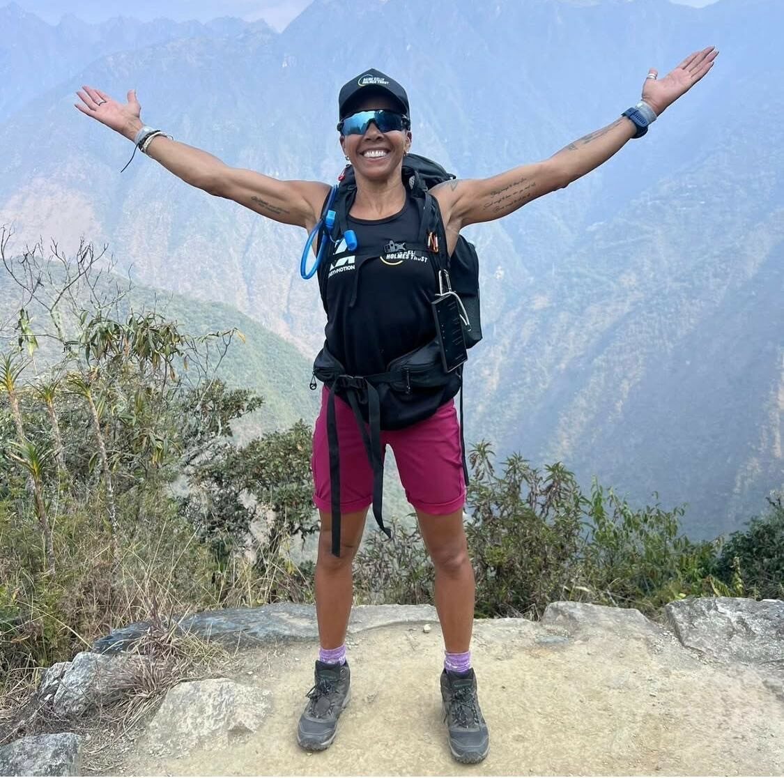 Kelly standing on a mountain holding her arms out to the side smiling.
