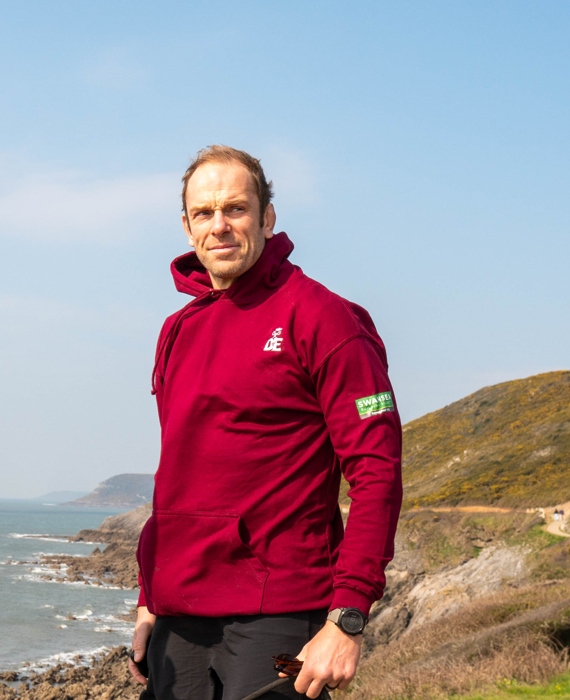 Alun Wyn wearing a red DofE hoodie standing on a mountain path.