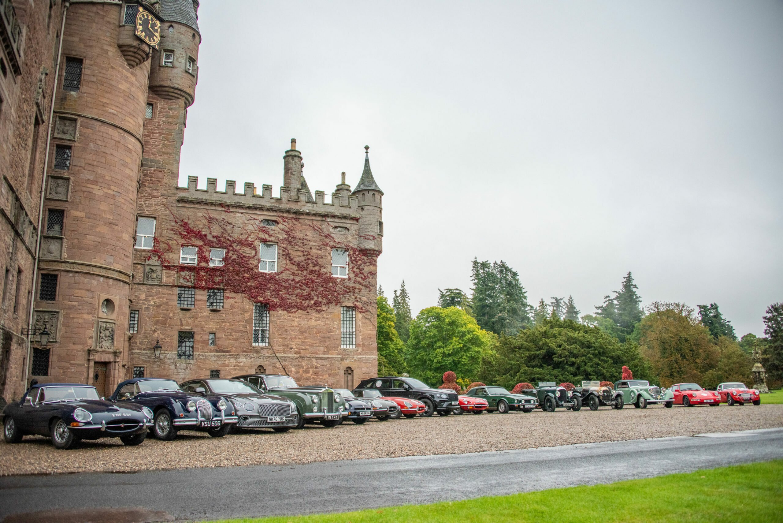 A line of classic cars parked in front of a castle.
