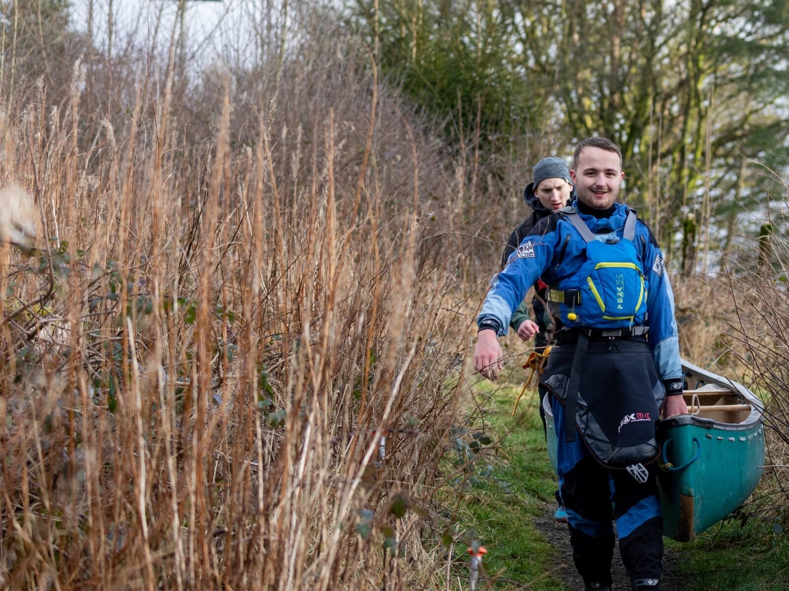 A young person is carrying their canoe through long grass.
