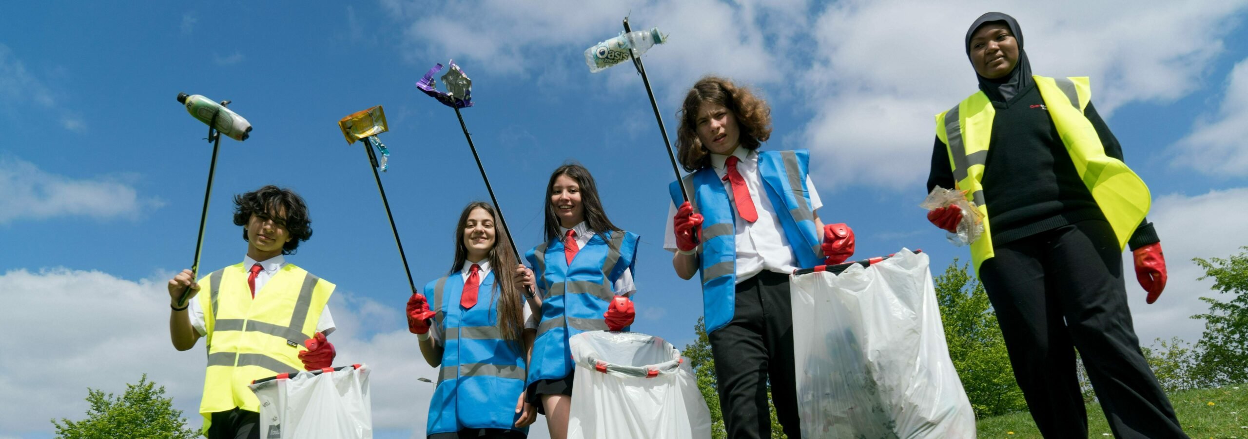 Five young people in high-vis and school uniforms litter picking outside.