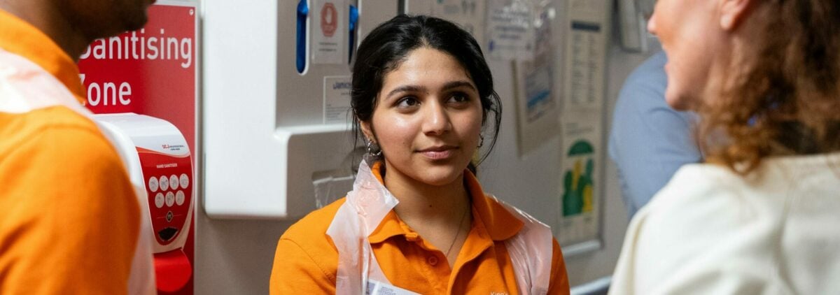 A D of E volunteer in a orange tshirt and plastic apron in a hospital.