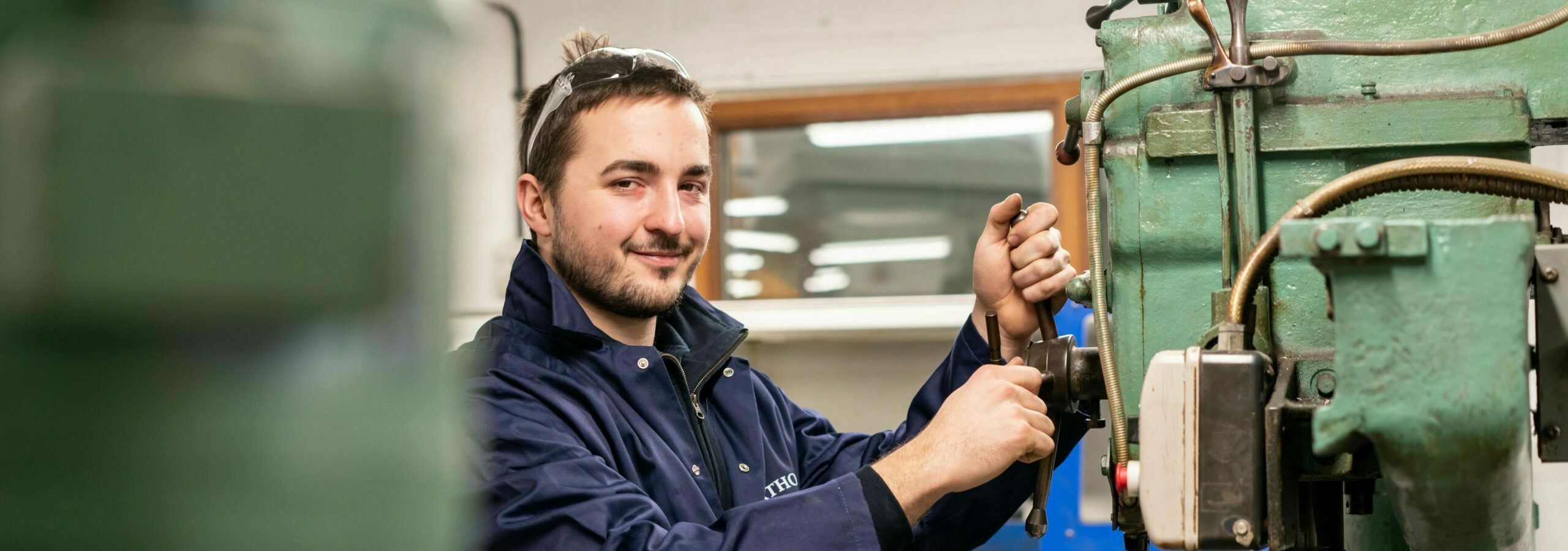 A young person wearing blue overalls working in a boat yard workshop.