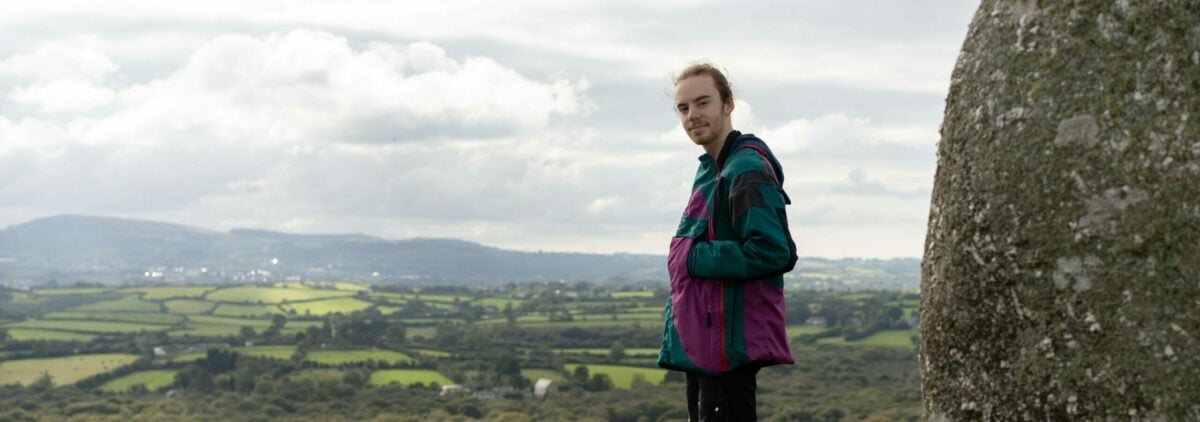 A young person standing on a rock in front of a view of green rolling hills.