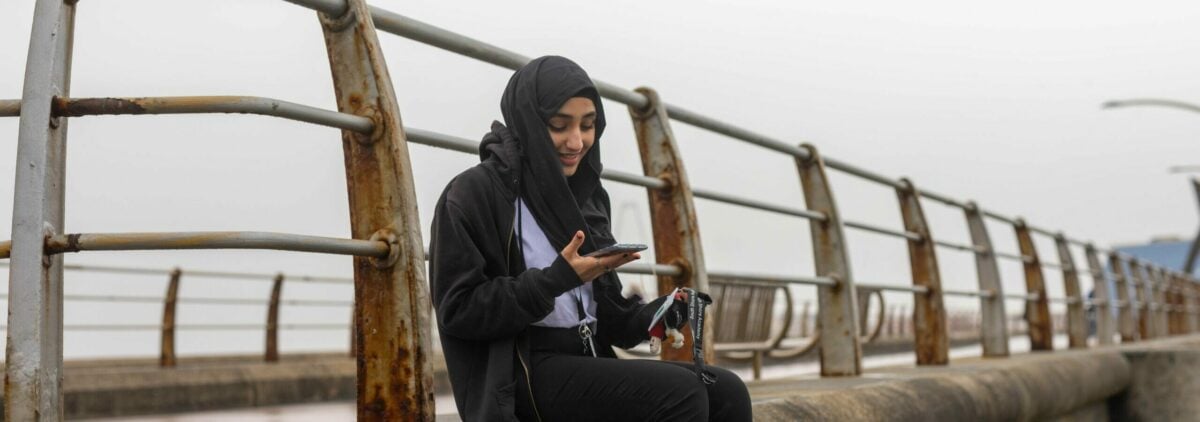 A young person sitting on a ledge looking at their phone.