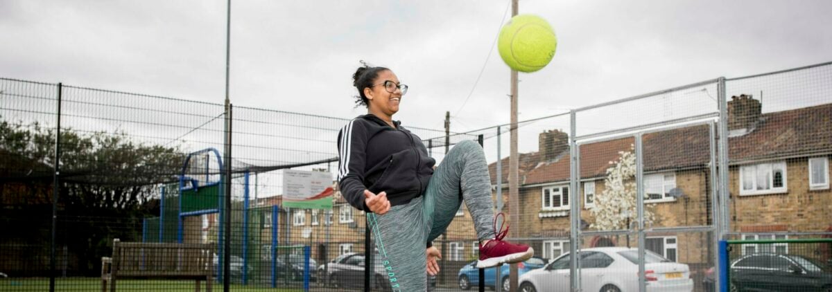 A young person playing football inside a football cage.