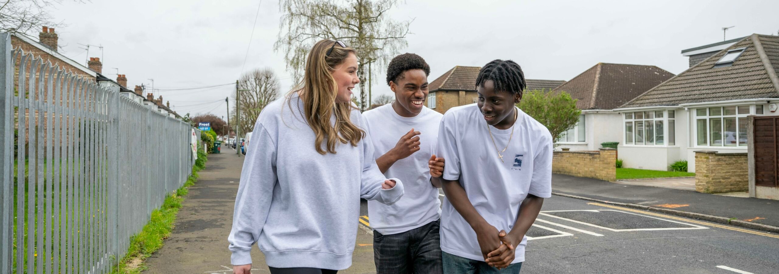 Three young people walking along the pavement talking to each other and laughing.