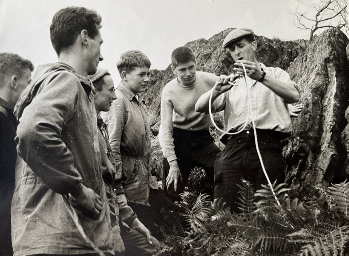 Black and white photo from the 50s showing a D of E leader teaching five boys how to tie a knot.