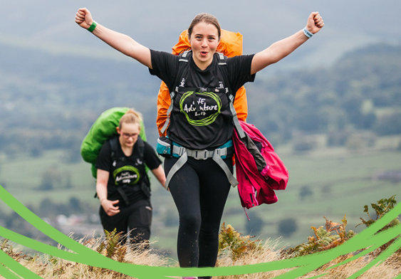 Two young people walking on their expedition, one raises their hands triumphantly in the air.