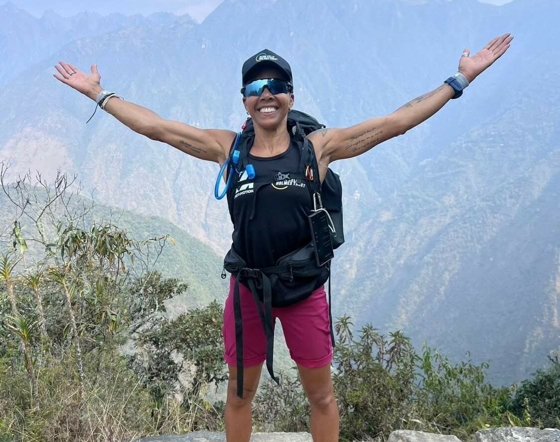 Kelly standing on a mountain holding her arms out to the side smiling.