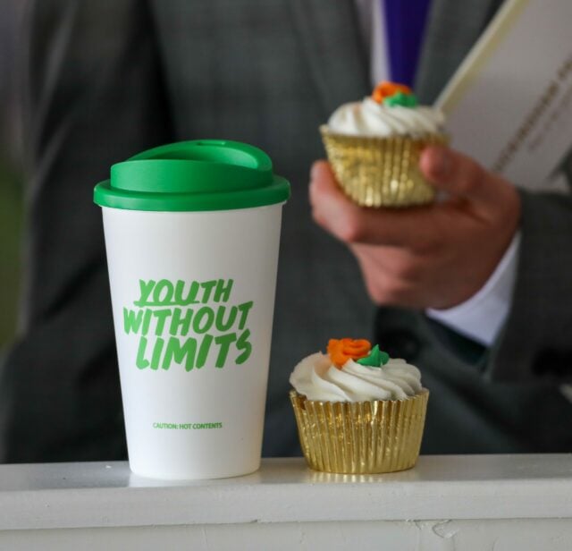 Alt text: Two coffee cups with green lids, one on the left and one on the right, both featuring the text 