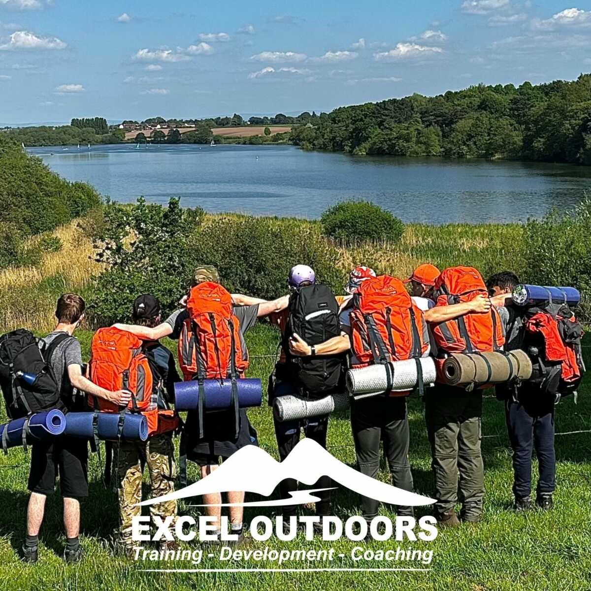 A group of young people on a DofE Expedition looking at a landscape view of rolling hills and a lake. White Excel Outdoors logo at the bottom.