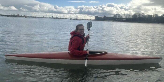 Anais smiles while sitting in a red kayak holding a paddle.