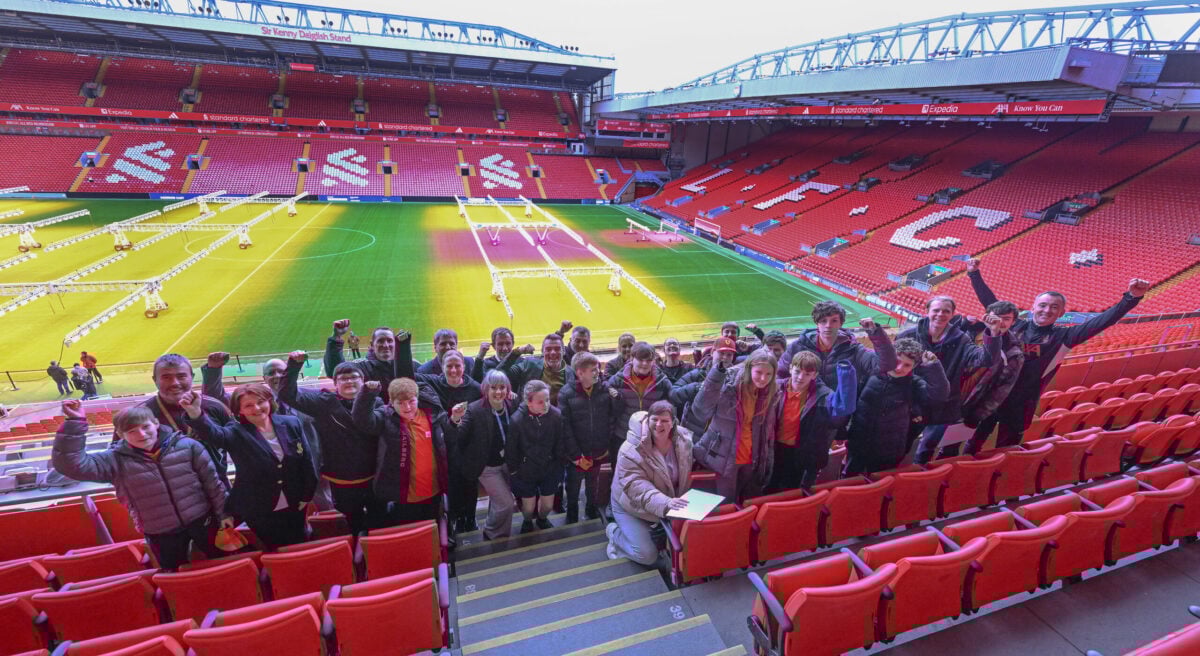 A group of people from D of E and L F C Foundation holding their hands up in celebration at Anfield football stadium.