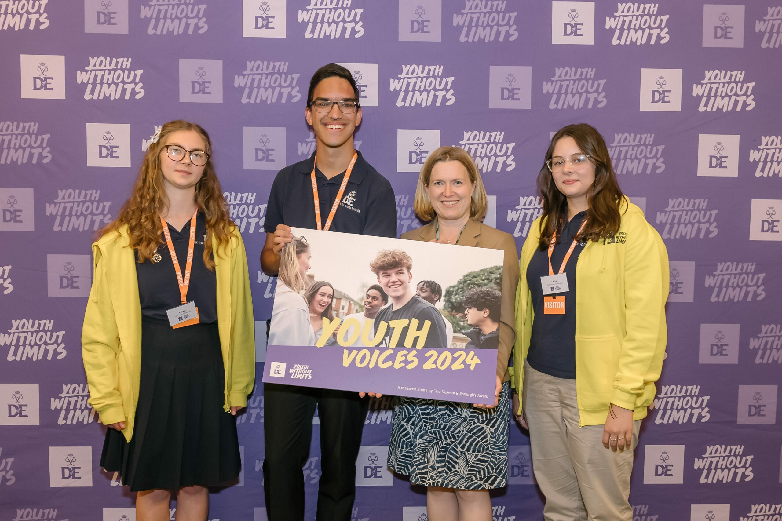 A group of four individuals stands in front of a purple backdrop that reads 