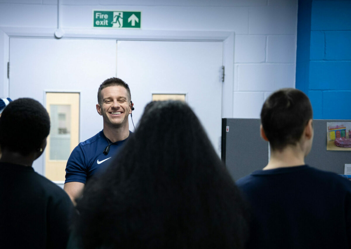 A smiling man in a blue shirt stands in front of four people who are facing him.