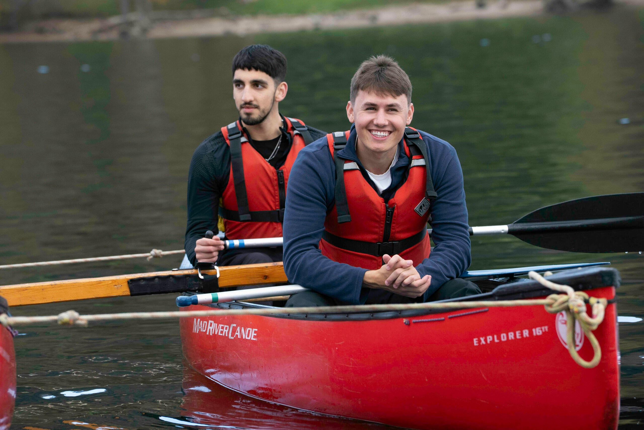 Two young people in a canoe wearing red lifejackets and smiling.