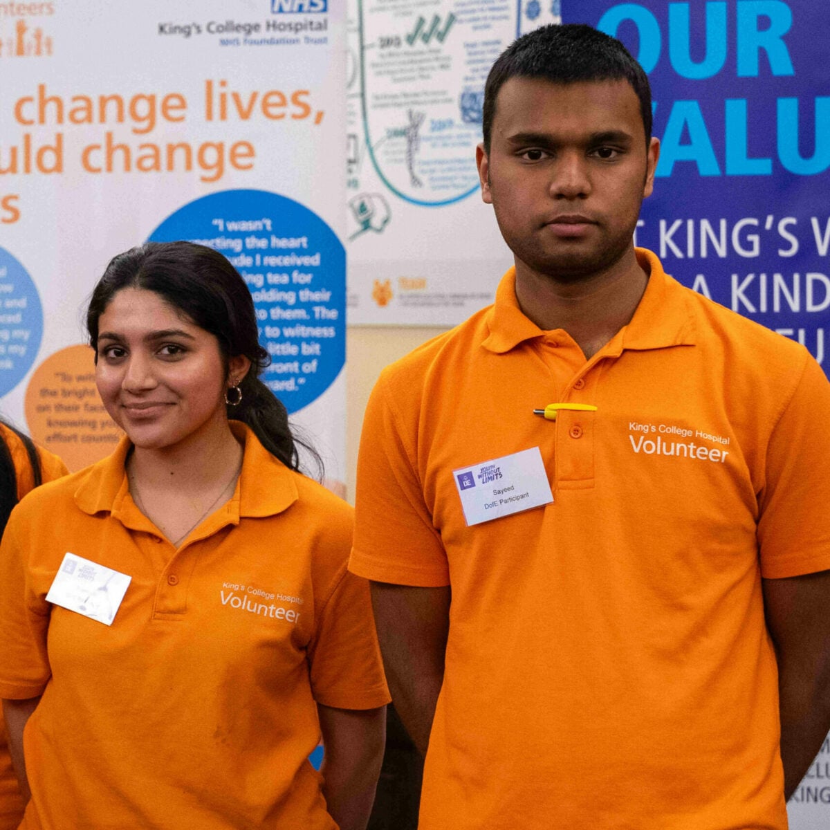 Two D of E volunteers at King's College hospital wearing orange tshirts standing in front of info posters.