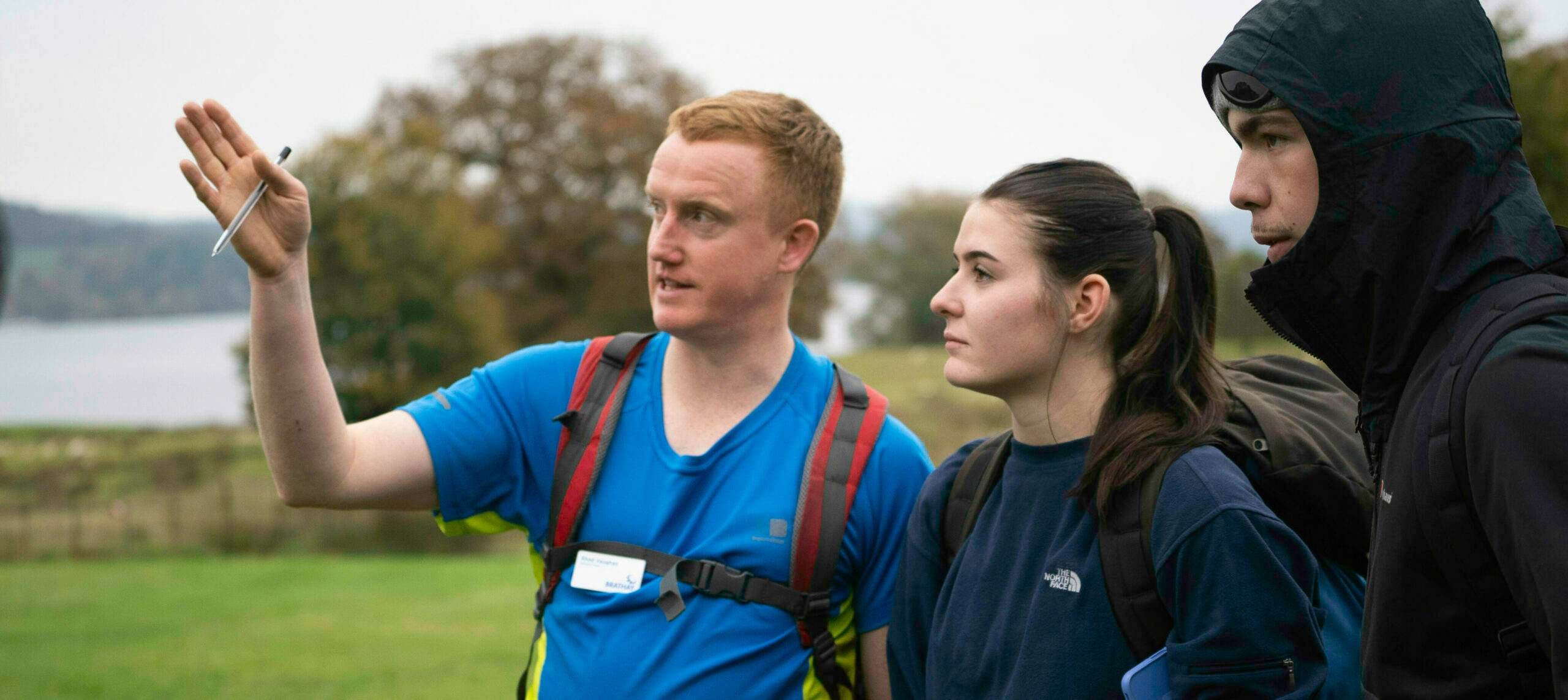 A Leader in a blue tshirt points ahead of himself and two young people standing next to him.