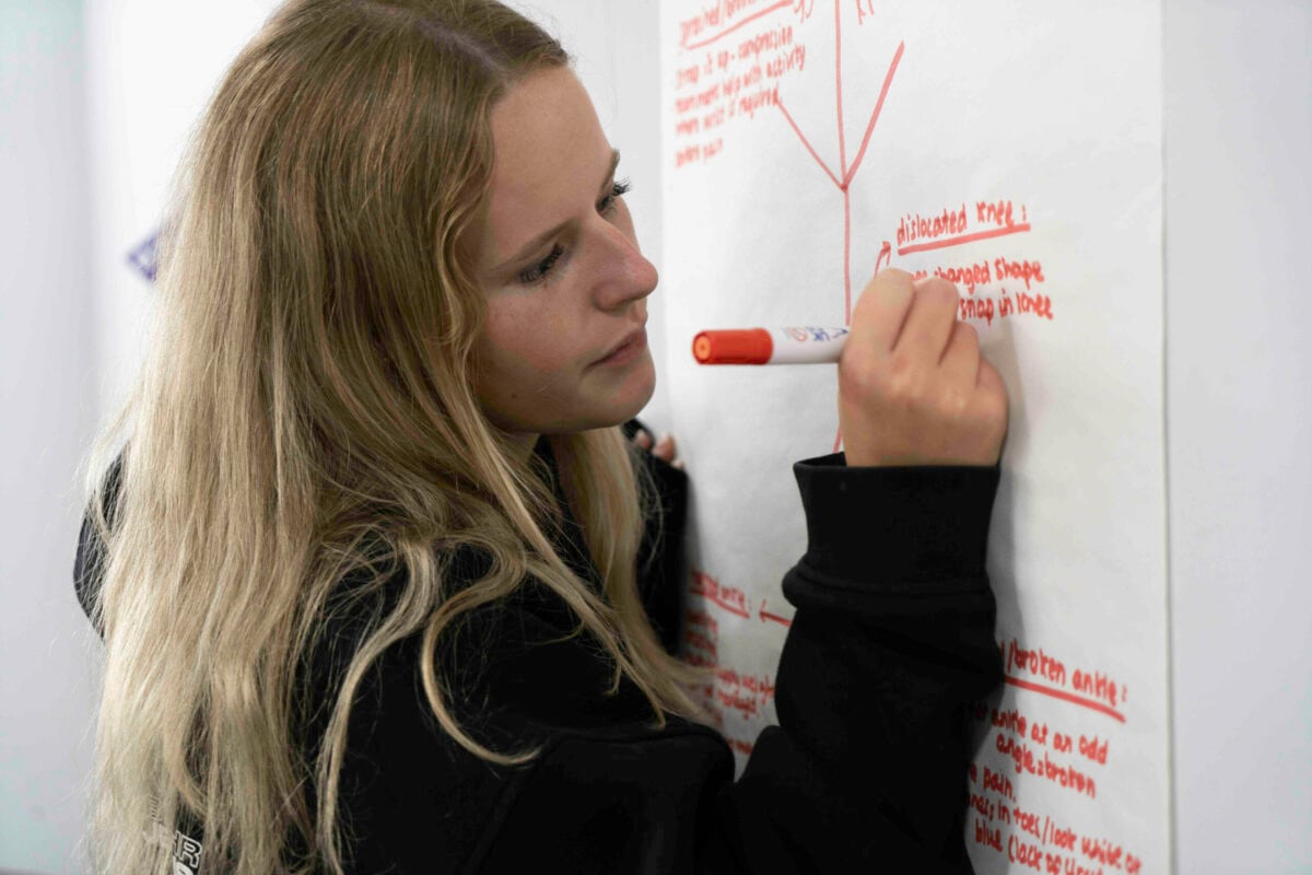 A young person writing on a big sheet of paper hanging on the wall with a red marker.