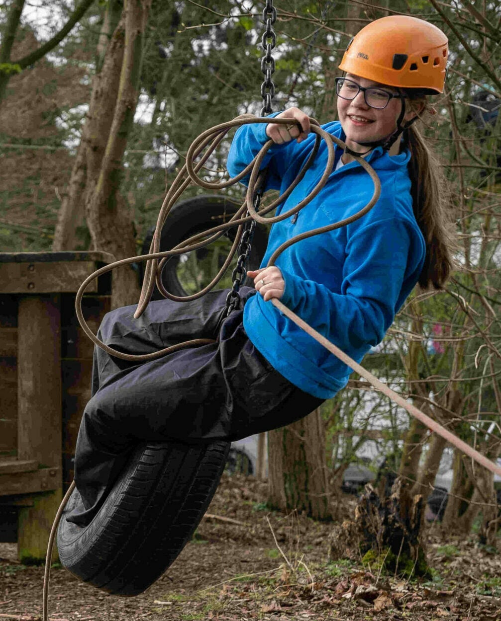 A young person wearing an orange helmet and blue coat standing in a tyre on an obstacle course.